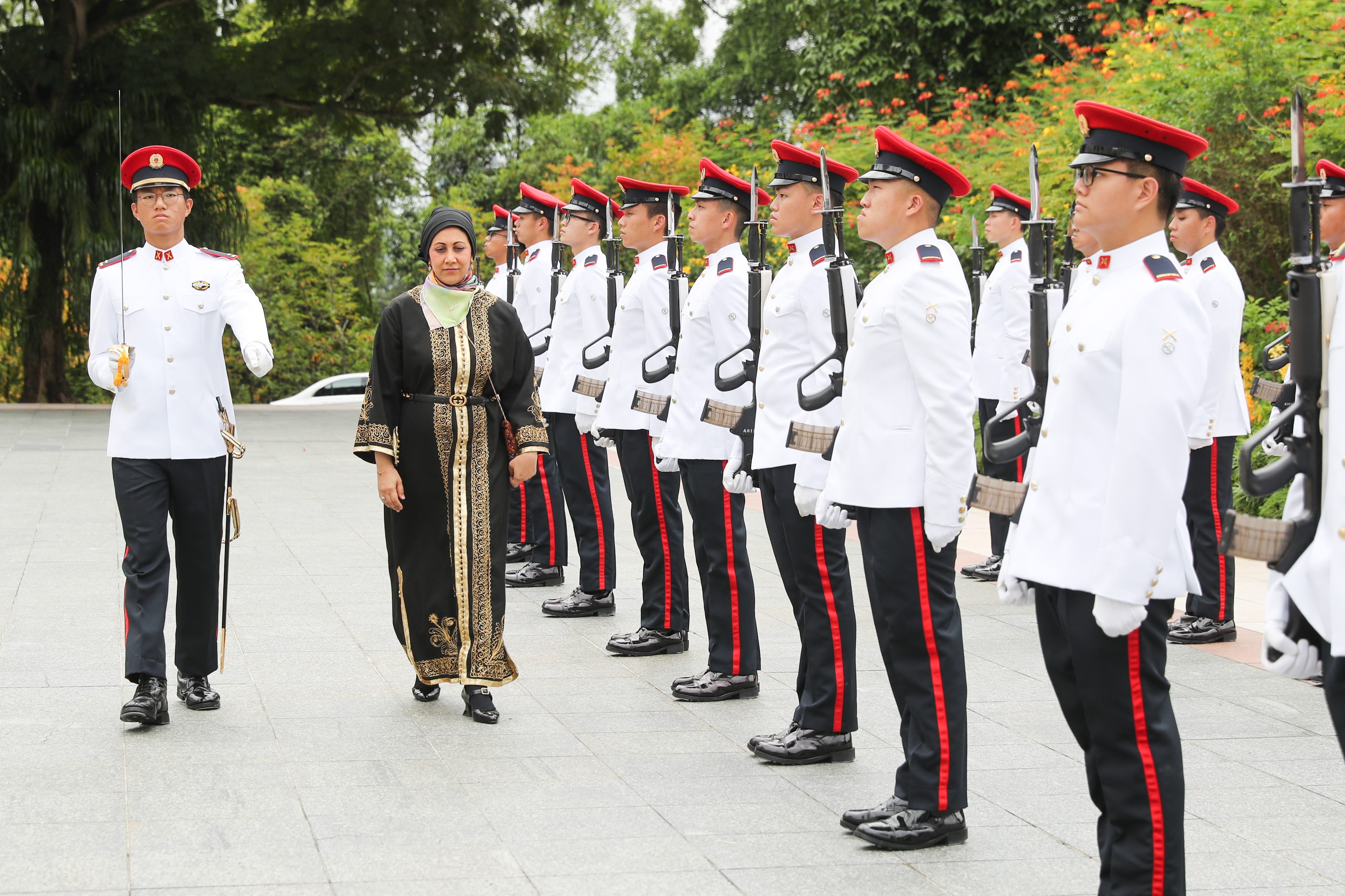 Line of soldiers in white uniforms and a woman in a black and gold dress.